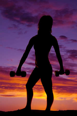 A silhouette of a woman working out with weights in the outdoors.の写真素材