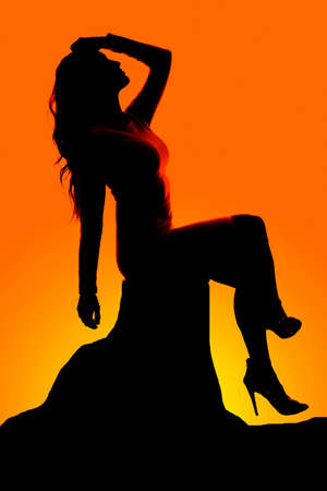 a silhouette of a woman sitting on a rock in her dress and heels.の写真素材