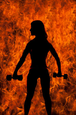 A silhouette of a woman with weights, with a fire background.の写真素材
