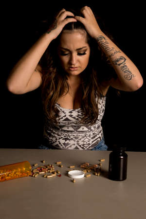 A troubled woman with her hands in her hair, looking at the drugs on the table.の写真素材