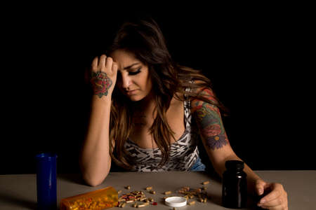 A woman with a depressed expression on her face, looking down at the drugs on the table.の写真素材