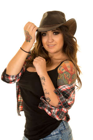 a cowgirl with her hand on her hat, and with her plaid shirt falling off of her shoulder, showing her tattoo.の写真素材