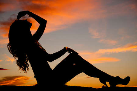 A silhouette of a woman sitting in her dress with her hand by her head.の写真素材