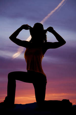 A silhouette of a woman kneeling holding on to her western hat.の写真素材