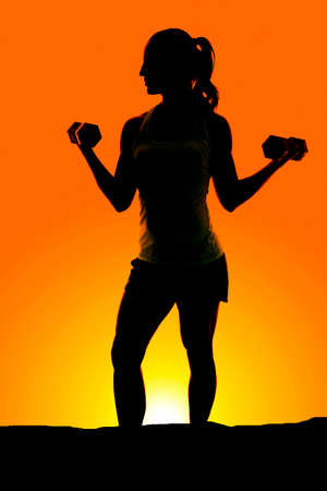 A silhouette of a woman working out in the outdoors with her weights.の写真素材
