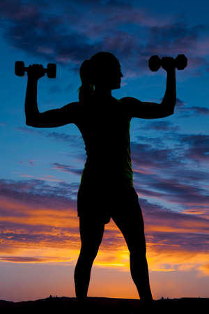 a silhouette of a woman flexing her arms, lifting weights.の写真素材