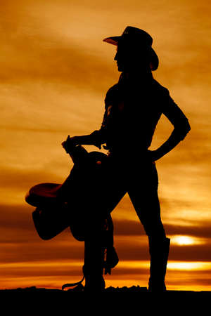 a silhouette of a woman holding on to her saddle, with her cowgirl hat on.の写真素材