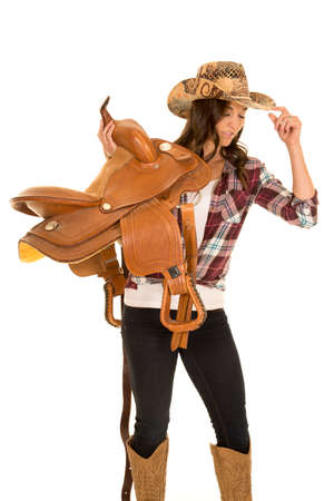 a cowgirl with her saddle on her shoulder, touching the brim of her hat.の写真素材