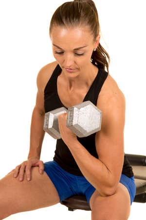 a woman sitting on a bench doing an arm curl with a weight.の写真素材