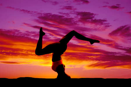 a silhouette of a woman doing a headstand in the outdoors.の写真素材