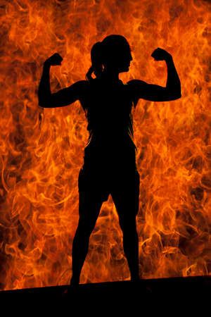 A silhouette of a woman flexing her arms with fire in the background.の写真素材