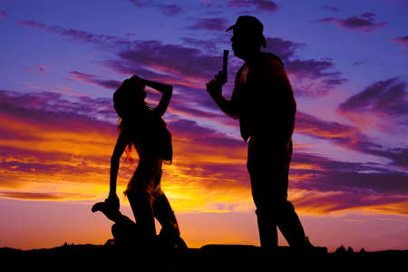 A silhouette of a woman kneeling on a saddle in front of her cowboy.の写真素材