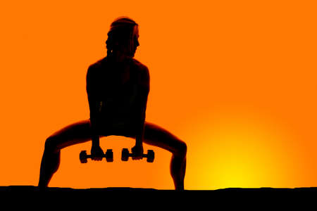 a silhouette of a woman doing a squat with weights in her hands.の写真素材
