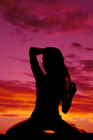 a silhouette of a woman kneeling playing with her hair.の写真素材