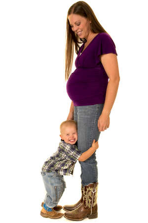 A pregnant woman with her little boy hugging her legs, in their western boots.の写真素材