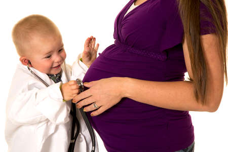 A young boy doctor in his lab coat, listening to the baby in his moms belly.の写真素材