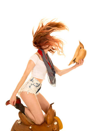A cowgirl kneeling on her saddle flipping her red hair with her hat in her hand.の写真素材