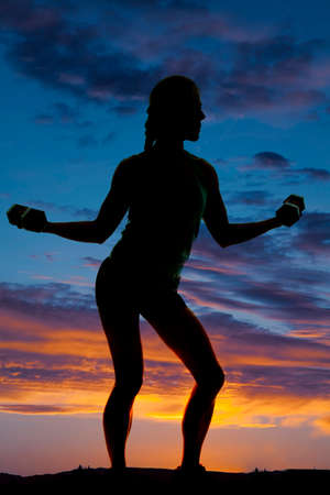 A silhouette of a woman working out with weights doing arm curls.の写真素材