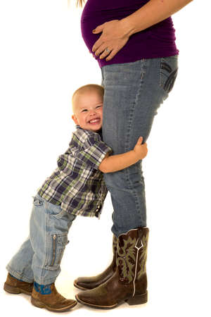 A pregnant woman with her little boy hugging her legs.の写真素材