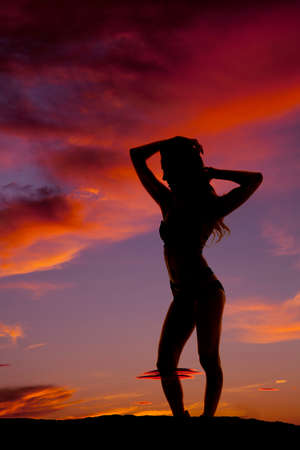 A silhouette of a woman standing with her hands in her hair.の写真素材