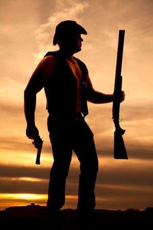A silhouette of a cowboy, with his pistol and shotgun in his hand ready for a fight.の写真素材