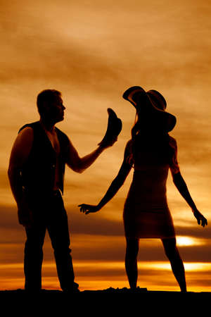 A silhouette of a cowboy taking off his hat for his lady, she is standing next to him.の写真素材