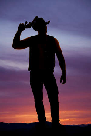 a silhouette of a cowboy with a pistol up by his western hat.の写真素材