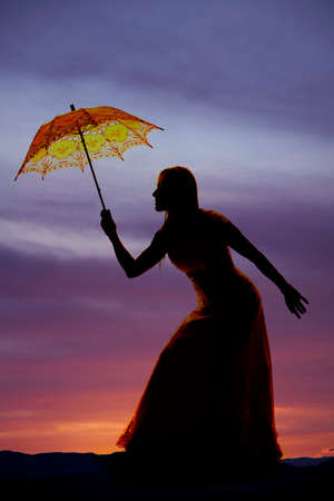 A silhouette of a woma bending over holding on to her umbrella.の写真素材