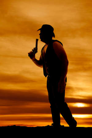 A silhouette of a cowboy blowing on the tip of his pistol in the outdoors.の写真素材