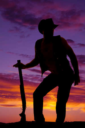 a silhouette of a cowboy with a funny body pose holding on to his shotgun.の写真素材