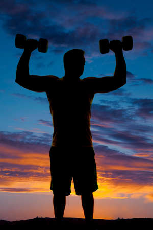 a silhouette of a man holding on to his weights doing shoulder presses.の写真素材