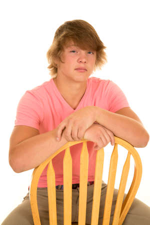 A teenage boy sitting on a chair looking with a serious expression on his face.の写真素材