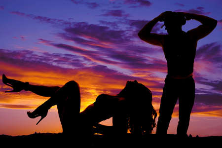 A silhouette of a woman laying on the ground with her back arched and her cowboy looking down at her.の写真素材