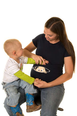 A little boy with a smile with his hands on his pregnant moms belly.の写真素材