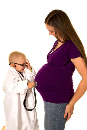 A young boy with a lab coat on, listening to his mom's pregnant belly with a stethoscope.の写真素材