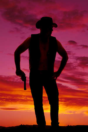A silhouette of a cowboy with a pistol in his hand looking to the side.の写真素材