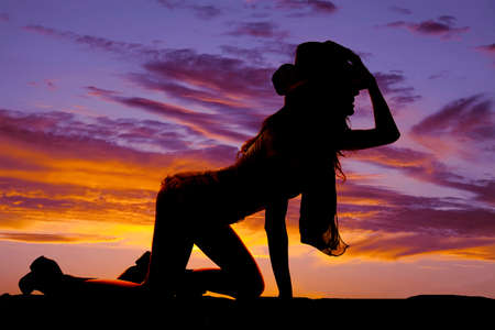a silhouette of a woman crawling on the ground, holding on to her western hat.の写真素材