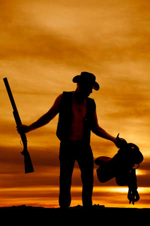 A silhouette of a cowboy holding on to his shotgun and saddle.の写真素材