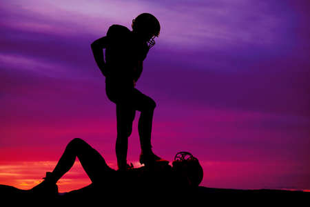 a silhouette of a player with is foot on top of another football player.の写真素材