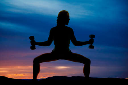 a silhouette of a woman in squat position, with weights in her hands.の写真素材