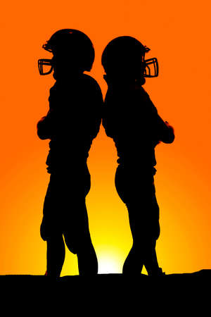 A silhouette of two football players standing back to back.の写真素材