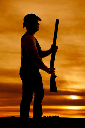 a silhouette of a cowboy holding on to his shotgun.の写真素材