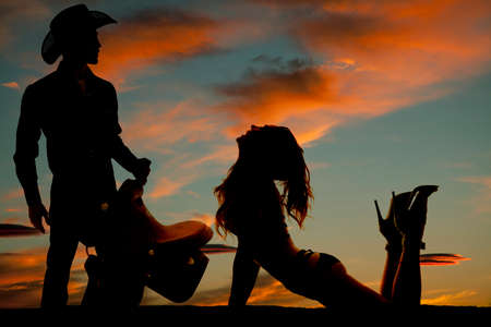 a silhouette of a woman arching her back with her cowboy standing next to her with his saddle.の写真素材