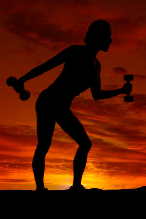 a silhouette of a woman working out in the outdoors with weightsの写真素材
