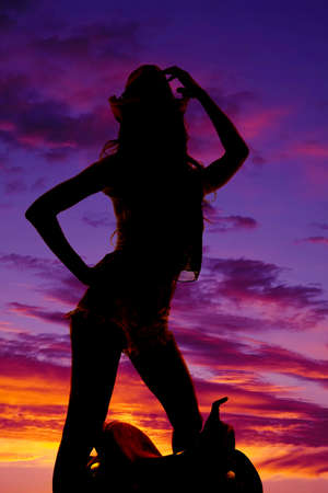 A silhouette of a cowgirl standing over a western saddle in the outdoorsの写真素材