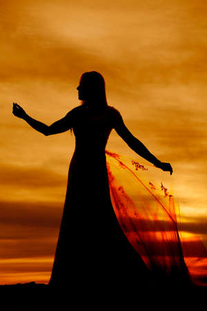 A silhouette of a woman in her wedding dress holding on to her train in the sunset.の写真素材