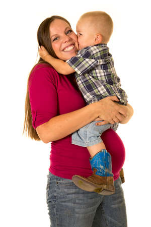 a pregnant woman with a big smile as she gets a kiss from her toddler boy.の写真素材
