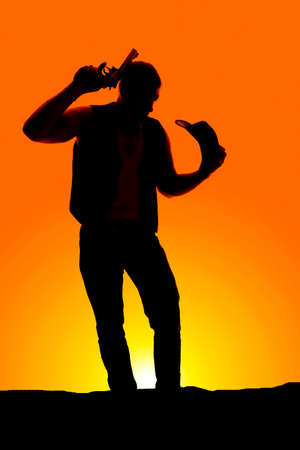 A silhouette of a cowboy with his western hat off his head, and a pistol by his head.の写真素材
