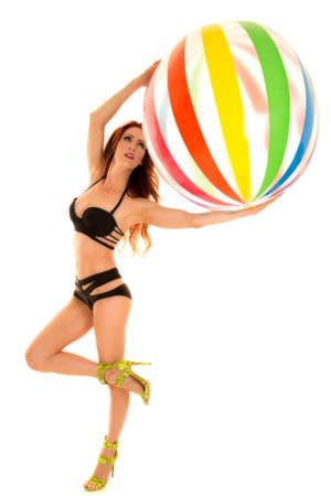 A woman in her bikini and high heel shoes playing with a big beach ball.の写真素材