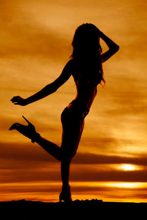 A silhouette of a woman standing, with a leg kicked up.の写真素材
